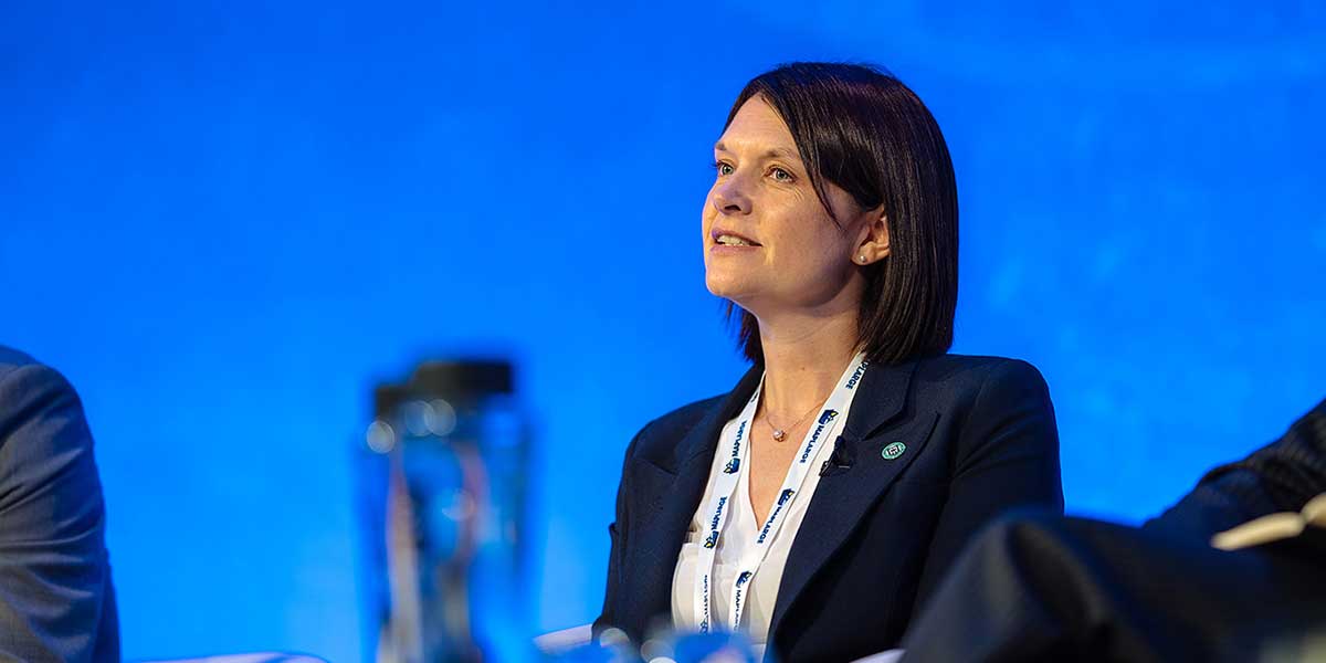 Dr Zena Wood at DGI Conference in London. She appears to be engaged in a conversation or listening attentively. A blurred object in the foreground suggests she is participating in a professional event or panel discussion.