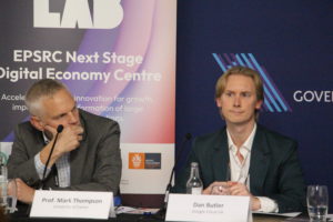 Prof. Mark Thompson from the University of Exeter sits thoughtfully, while Dan Butler from Google Cloud UK listens during a panel discussion.